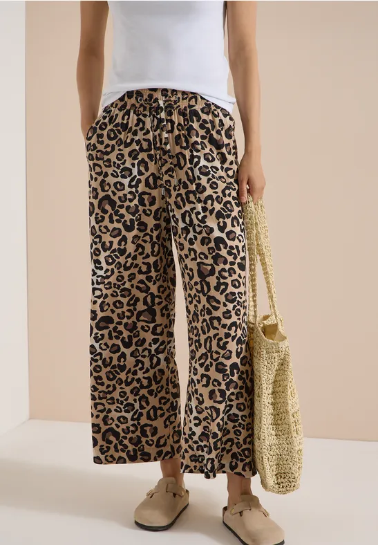 Femme portant un pantalon large léopard, un haut blanc et un sac en paille.
