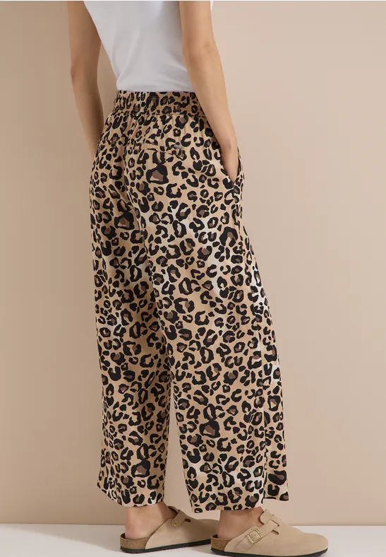 Femme en t-shirt blanc et pantalon large imprimé léopard, de profil sur fond beige.