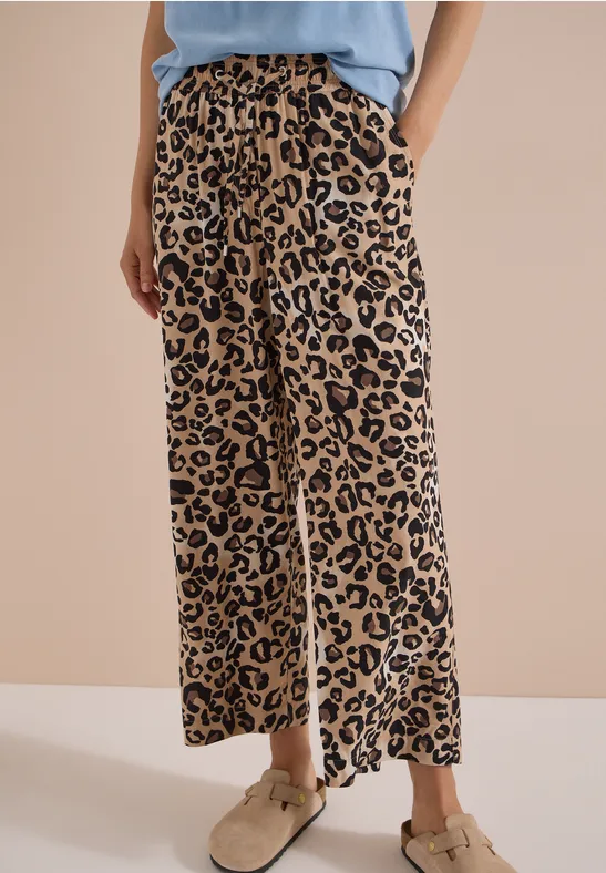 Femme en pantalon ample à motif léopard beige et noir, coupe décontractée avec poches latérales.