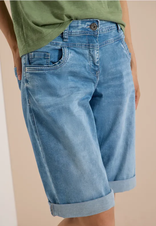 Person trägt grünes T-Shirt und hellblaue Jeans-Bermuda mit umgeschlagenem Saum.