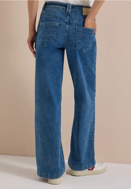 Vue de dos d’une personne portant un jean bleu large en denim, poches plaquées et coupe droite.