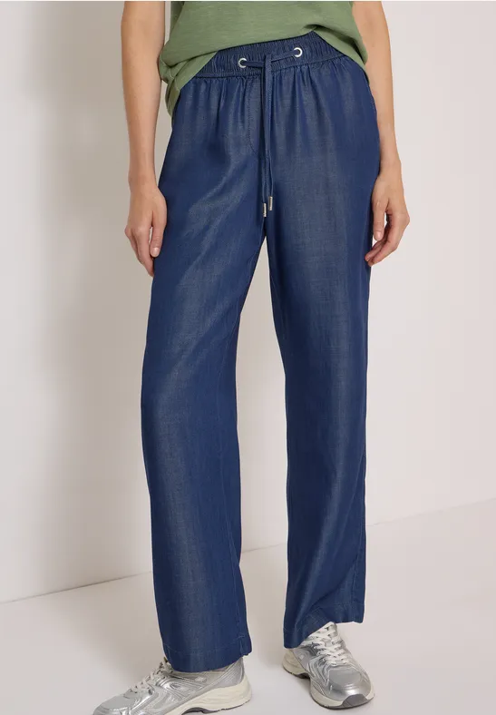 Pantalon bleu ample à cordon de serrage, porté avec des baskets argentées.