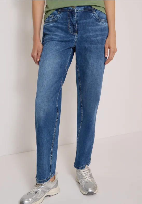 Eine Person trägt blaue Jeans und silberne Sneaker vor neutralem Hintergrund.