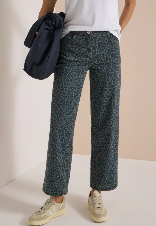 Weite, gemusterte Hose mit grünem Print, kombiniert mit weißen Sneakern, weißem T-Shirt und blauer Umhängetasche.