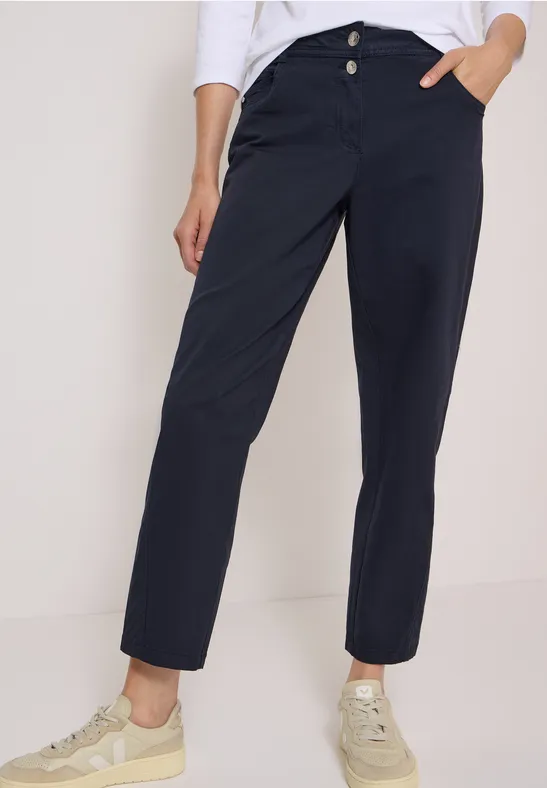 Dunkelblaue, gerade geschnittene Hose mit zwei Knöpfen, seitlichen Taschen und hellen Sneakern.