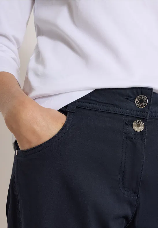 Person in weißem Oberteil steckt Hand in Hosentasche einer dunkelblauen Hose.