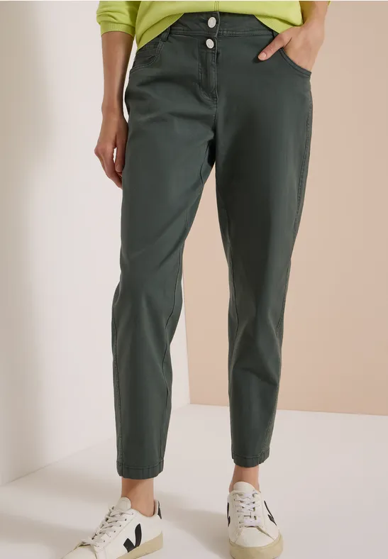 Eine Person trägt schmal zulaufende, dunkelgrüne Chino-Hose und weiße Sneaker.