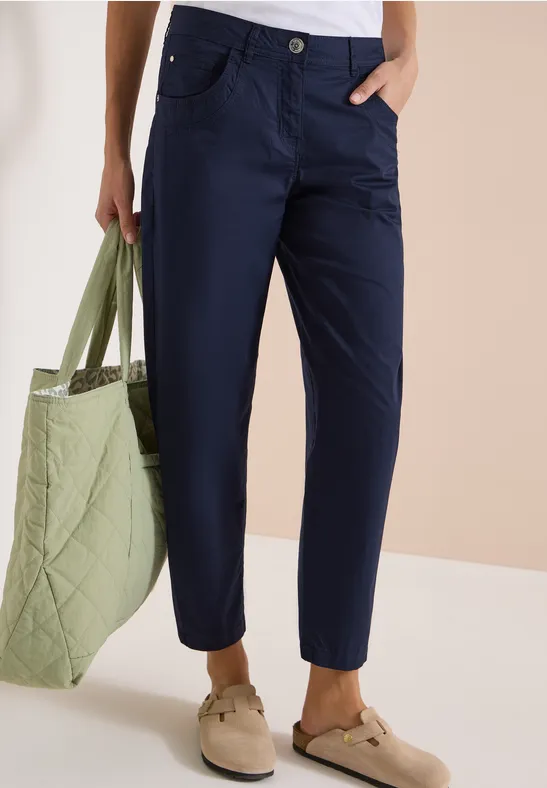 Person trägt dunkelblaue Hose, hält gesteppte grüne Tasche, dazu bequeme beige Schuhe.