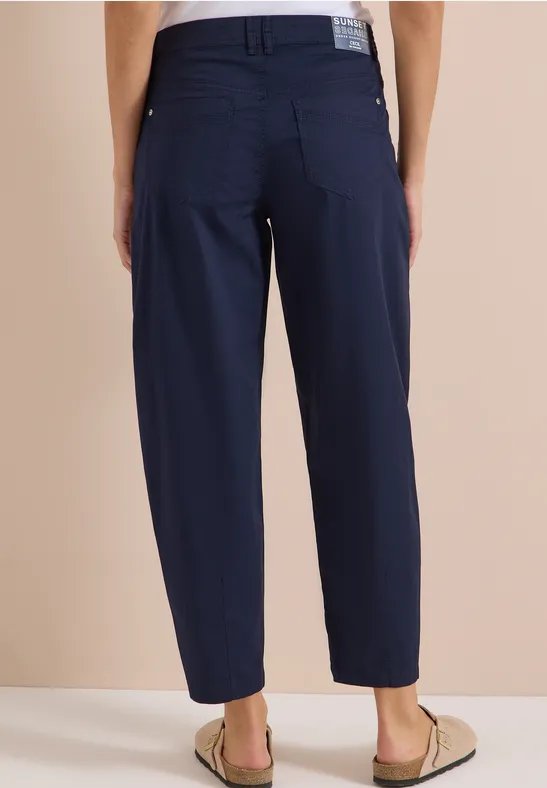 Person steht von hinten, trägt eine marineblaue, locker sitzende Hose bis zu den Knöcheln und Sandalen.