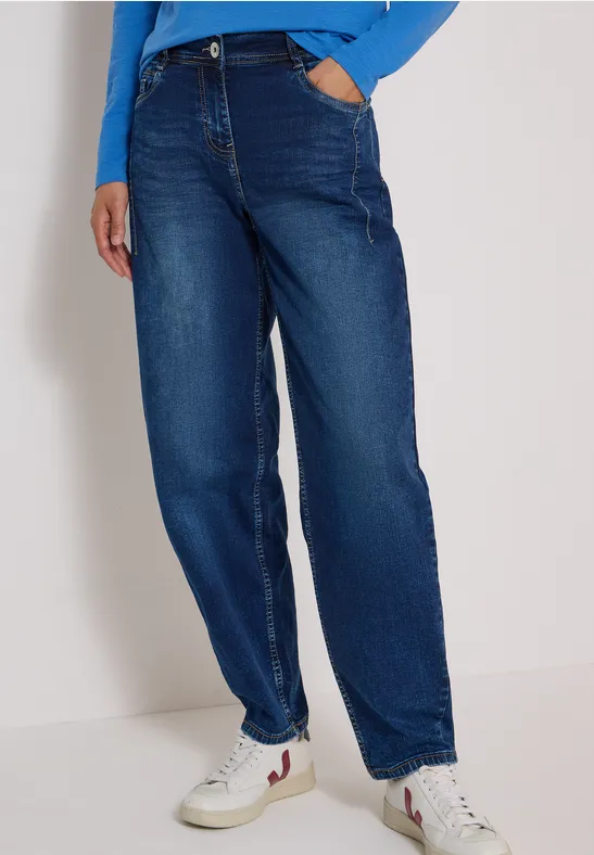 Beine in hoch geschnittener, weiter dunkelblauer Jeans und weißen Sneakern.
