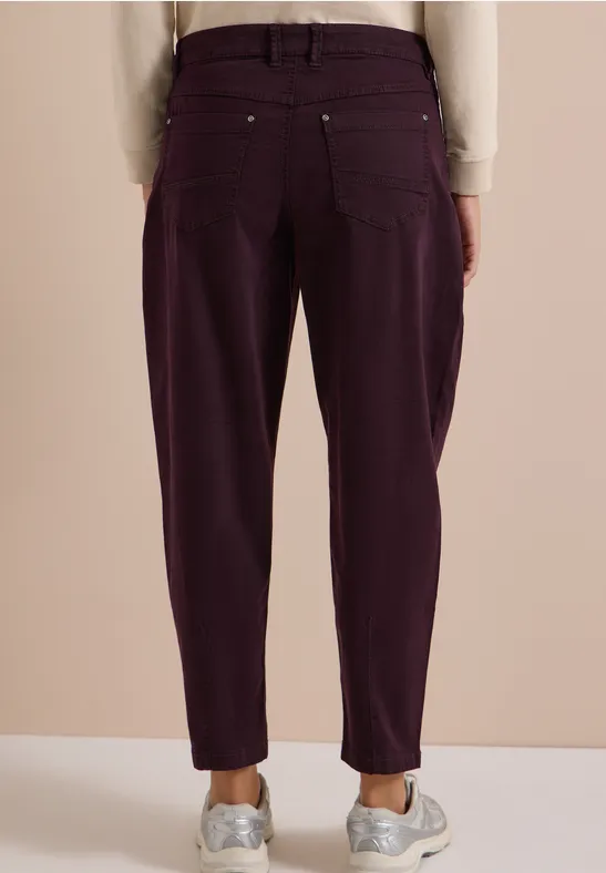 Vue arrière d'une personne portant un pantalon taille haute violet foncé et des baskets blanches.