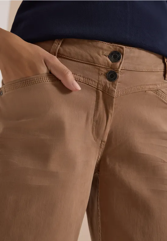 Pantalon marron à deux boutons, main glissée dans la poche latérale.
