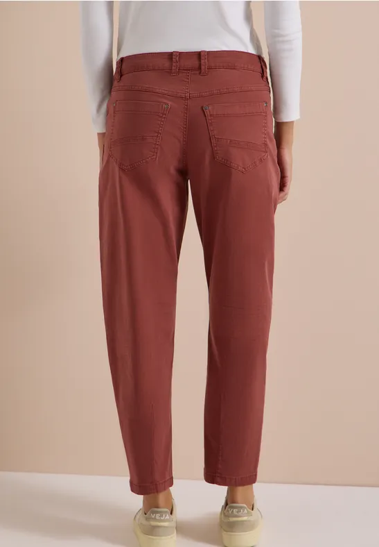 Vue de dos d’une personne portant un pantalon bordeaux ample à poches devant un fond neutre.