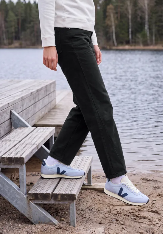 Personne en pantalon noir et baskets blanches sur un escalier en bois au bord d’un lac.