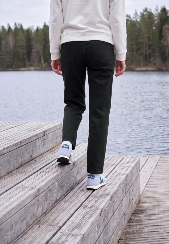 Personne en pantalon noir et baskets blanches marchant sur une plateforme en bois au bord d’un lac.