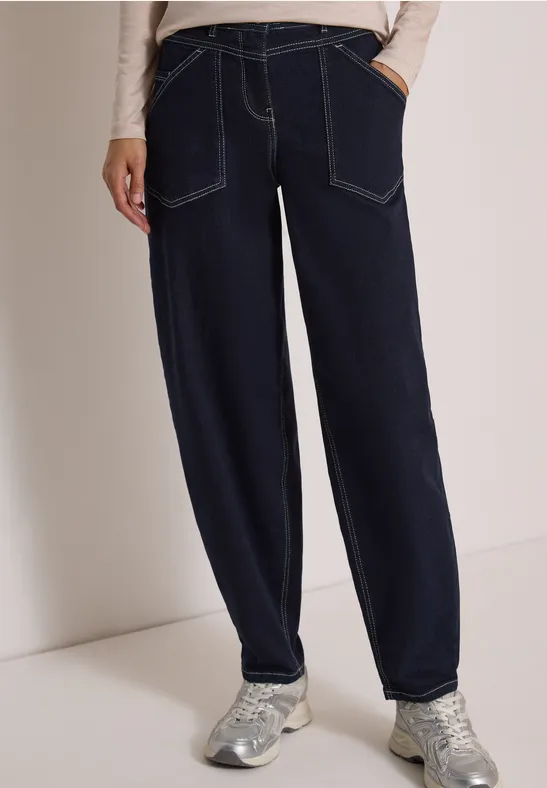 Dunkelblaue, locker sitzende Jeans mit Kontrastnähten und silbernen Sneakern.