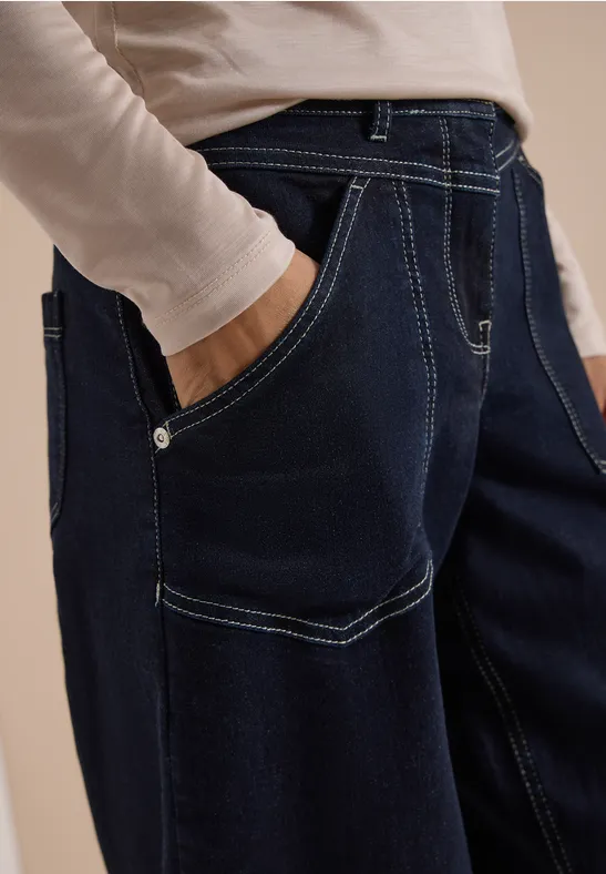 Dunkelblaue Jeans mit kontrastierenden Nähten und Hand in der Tasche.