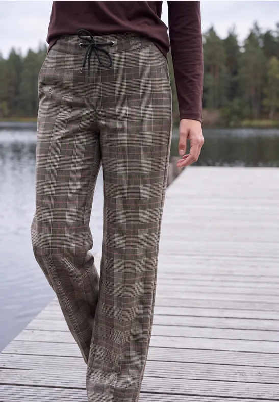 Une personne debout sur une jetée en bois au bord d’un lac porte un pantalon ample à carreaux avec cordon.