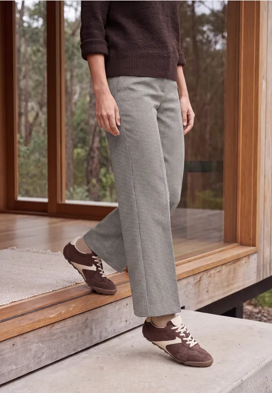 Une personne en pantalon gris et baskets brunes descend d'une plateforme en bois en plein air.