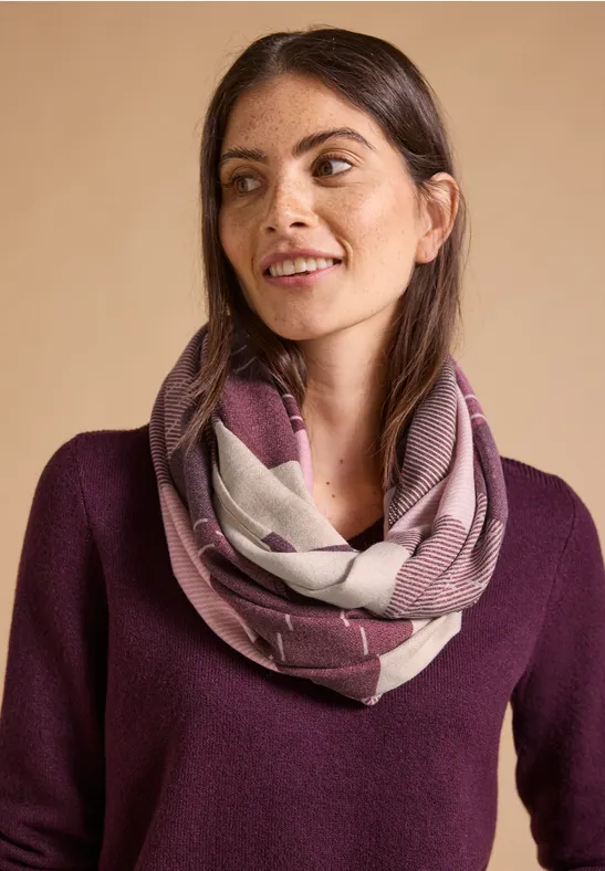 Vrouw met donker haar draagt een gemêleerde loopsjaal en een paars truitje, glimlacht zacht.