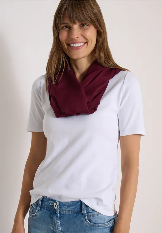 Lächelnde Frau in weißem T-Shirt, blauen Jeans und weinrotem Schal.