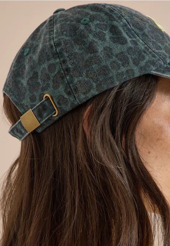 Profil d'une femme aux cheveux bruns portant une casquette sombre à motif léopard.