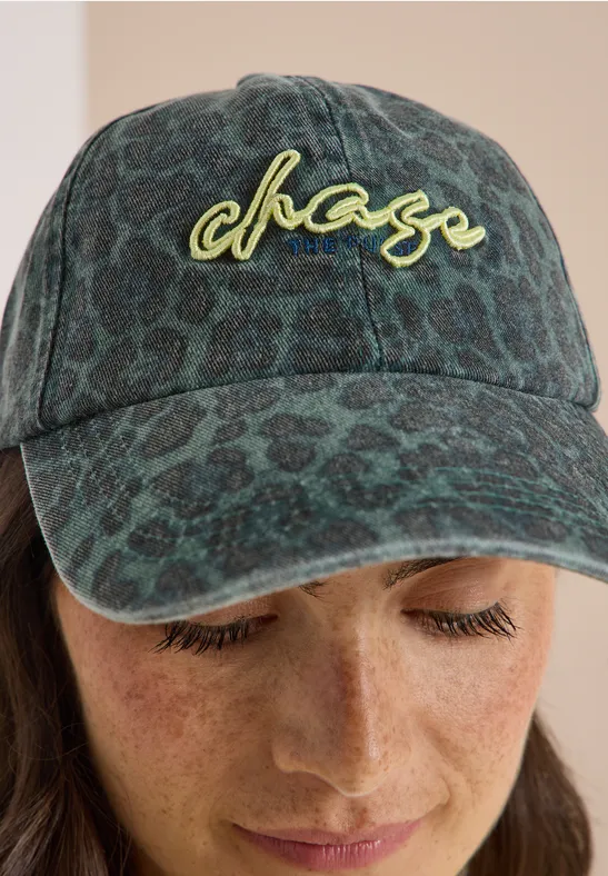 Femme aux yeux baissés portant une casquette verte à motif chase et des taches de rousseur.