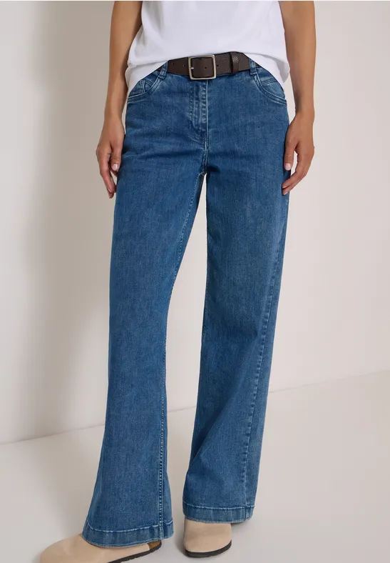 Une personne porte un jean bleu taille haute légèrement évasé avec ceinture.