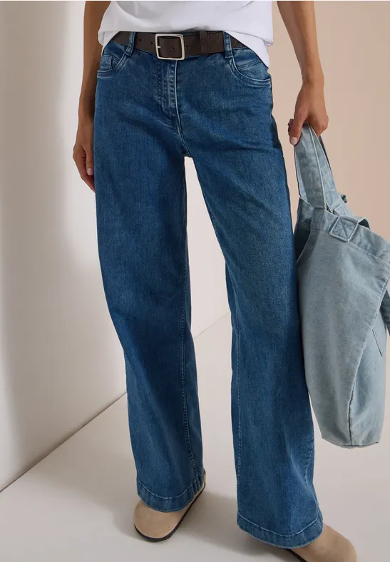 Personne porte un jean large bleu avec ceinture et tient un sac clair en denim.