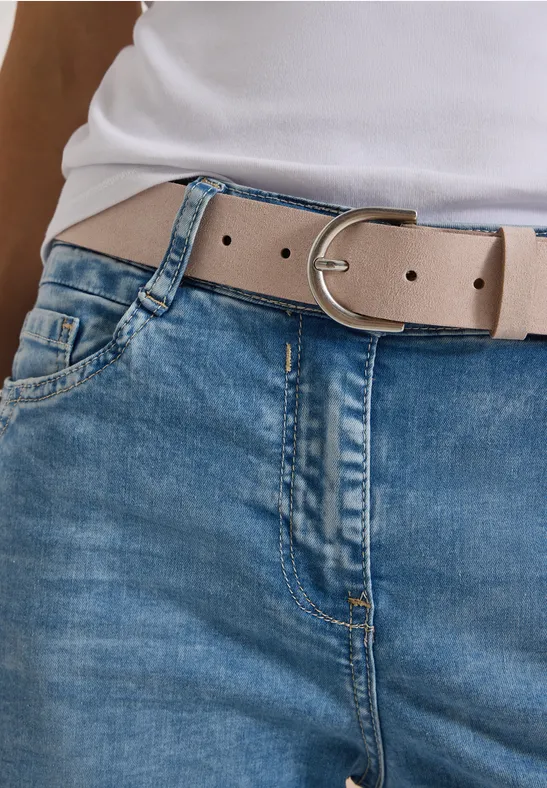 Vue de la taille avec une ceinture beige clair à boucle argentée, un jean bleu et un haut blanc.