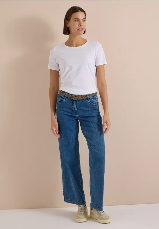 Femme en t-shirt blanc, jean large et baskets devant un fond beige