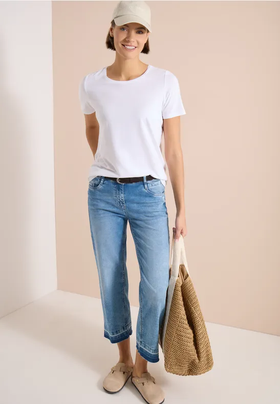 Femme en t-shirt blanc, jean bleu, mocassins beiges et grand sac en osier.