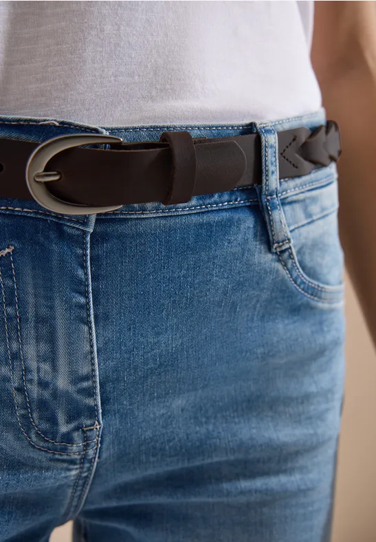 Gros plan sur un jean bleu ceinturé d’une tresse marron avec un haut blanc.