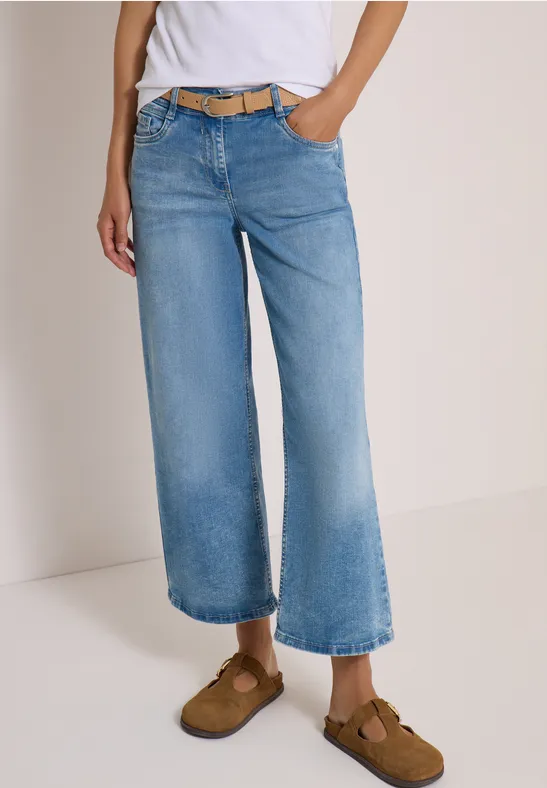 Personne porte un jean large coupe culotte, ceinturé, jusqu'aux chevilles, avec mocassins marron, fond neutre.