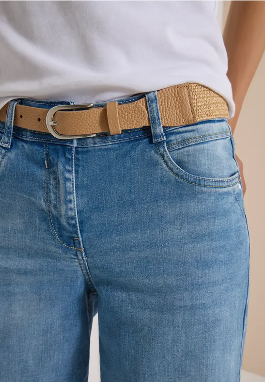 Gros plan sur un jean bleu porté à la taille, agrémenté d'une ceinture tressée beige.