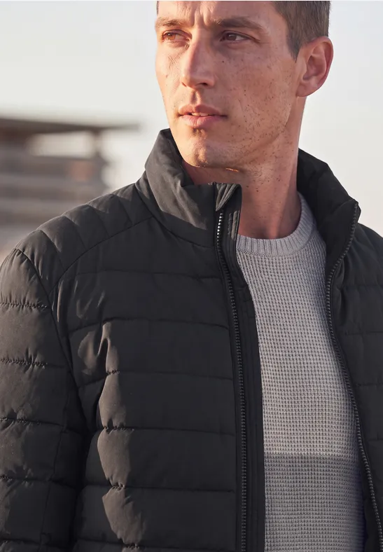 Ein Mann in einer schwarzen Steppjacke und grauem Pullover blickt in die Ferne.