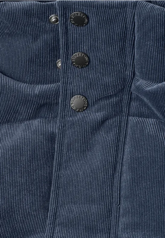 Nahaufnahme eines dunkelblauen Cordstoff-Bekleidungsstücks mit vertikalen Nähten und drei Metall-Druckknöpfen.