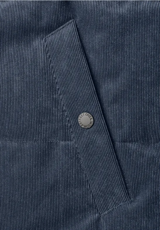 Nahaufnahme eines dunkelblauen Cordstoffs mit Taschenklappe und Metall-Druckknopf.