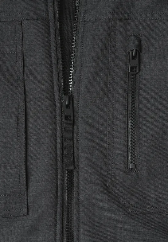 Vue rapprochée d'une veste noire, fermeture éclair visible et poche à soufflet oblique.