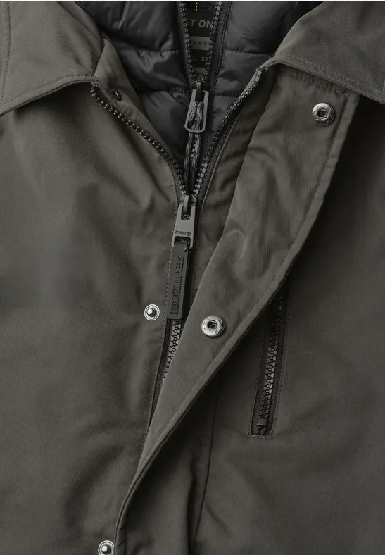 Nahaufnahme einer dunkelgrünen Jacke mit Reißverschluss, Druckknöpfen und wattierter Innenlage.