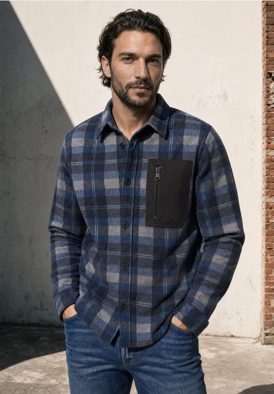 Mann mit kariertem Flanellhemd und Jeans, Hände in den Taschen, vor hellem Hintergrund.