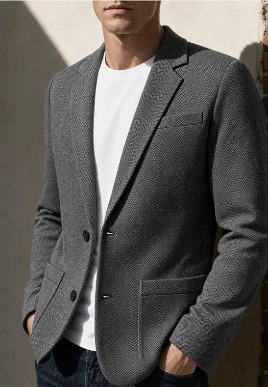 Mann trägt grauen Blazer und weißes T-Shirt, Hände in den Taschen