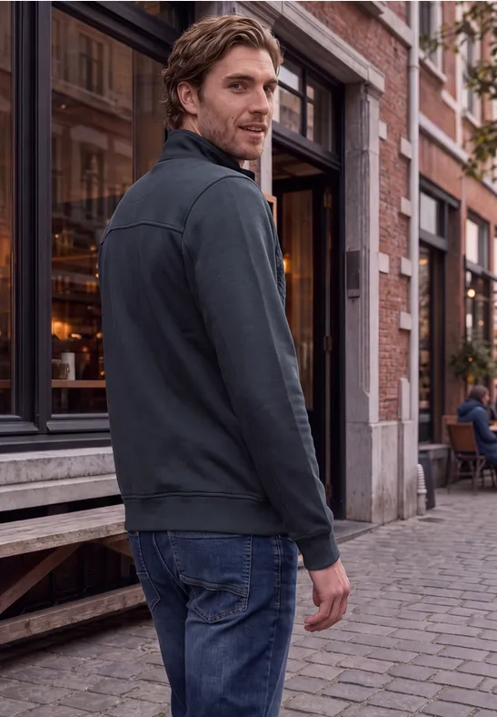 Ein Mann in Jeans und Jacke läuft auf einer kopfsteingepflasterten Straße an Cafégässchen vorbei und blickt zurück.