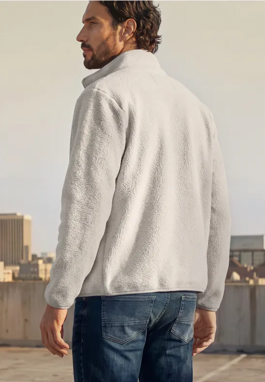 Mann von hinten in grauer Fleecejacke auf Dach mit Stadt im Hintergrund.