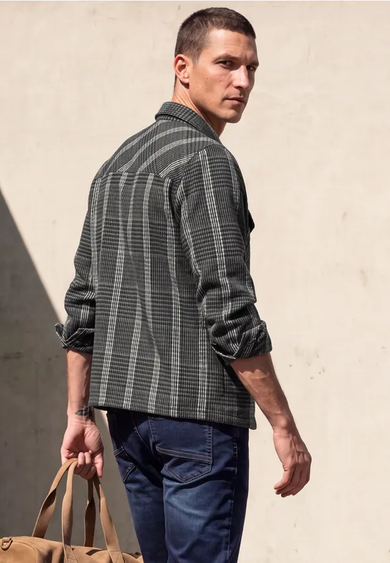 Ein Mann in gestreiftem Hemd und Jeans trägt eine Tasche und blickt zurück.