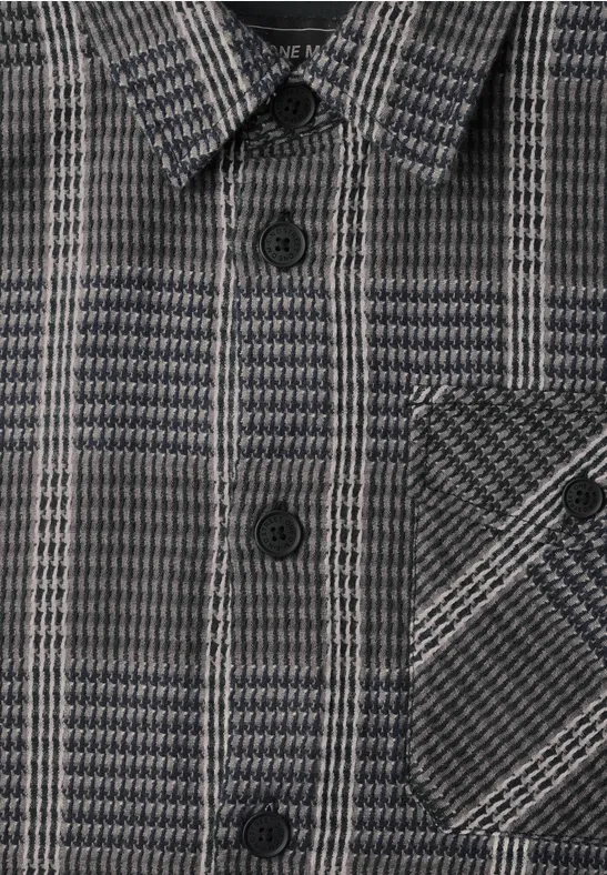 Nahaufnahme einer grauen Jacke mit Hahnentritt-Muster, Knöpfen und Brusttasche.