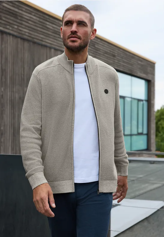 Ein Mann steht vor einem modernen Gebäude und trägt eine bequeme, hellgraue Zip-Jacke über weißem T-Shirt.