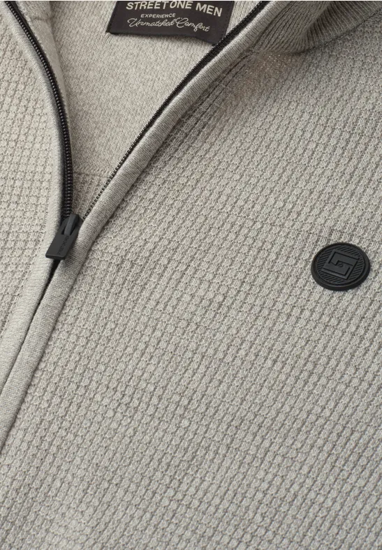 Grauer, grob strukturierter Pullover mit Reißverschluss und kleinem Logo-Patch.