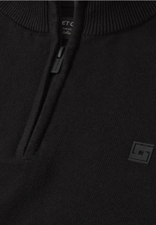 Schwarzer Strickpullover mit kurzem Reißverschluss und kleinem Logo-Patch vorne.