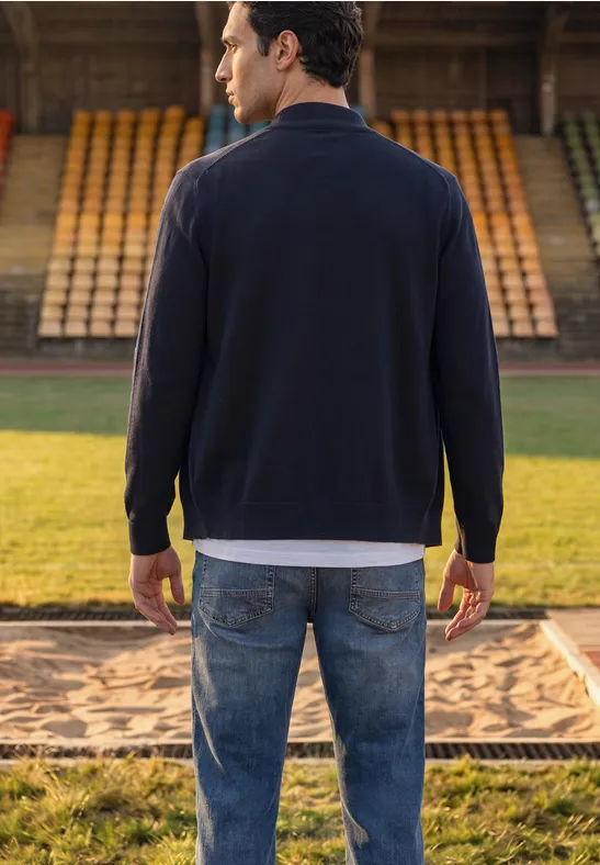 Ein Mann steht mit dem Rücken zur Kamera in Jeans und Pullover auf einer Bahn mit Sandmulde im Stadion.